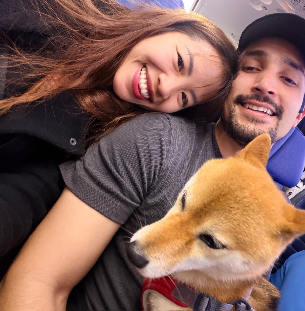 Trinique and Juan Pablo smiling in an airplane seat with Amie the Shiba Inu on their laps